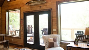 A spacious room with wooden walls, large windows, a round table, a chair, and a wooden cabinet.