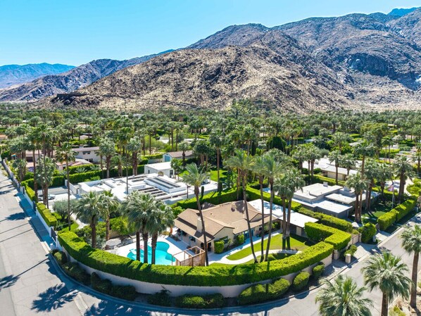 A resort with a pool, palm trees, and mountains in the background.