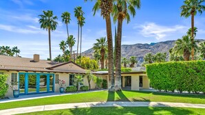 Una casa residencial con un césped cuidado, palmeras y una montaña al fondo.