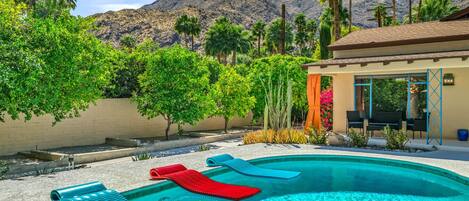 A swimming pool with lounge chairs, a pergola, and a mountain backdrop.