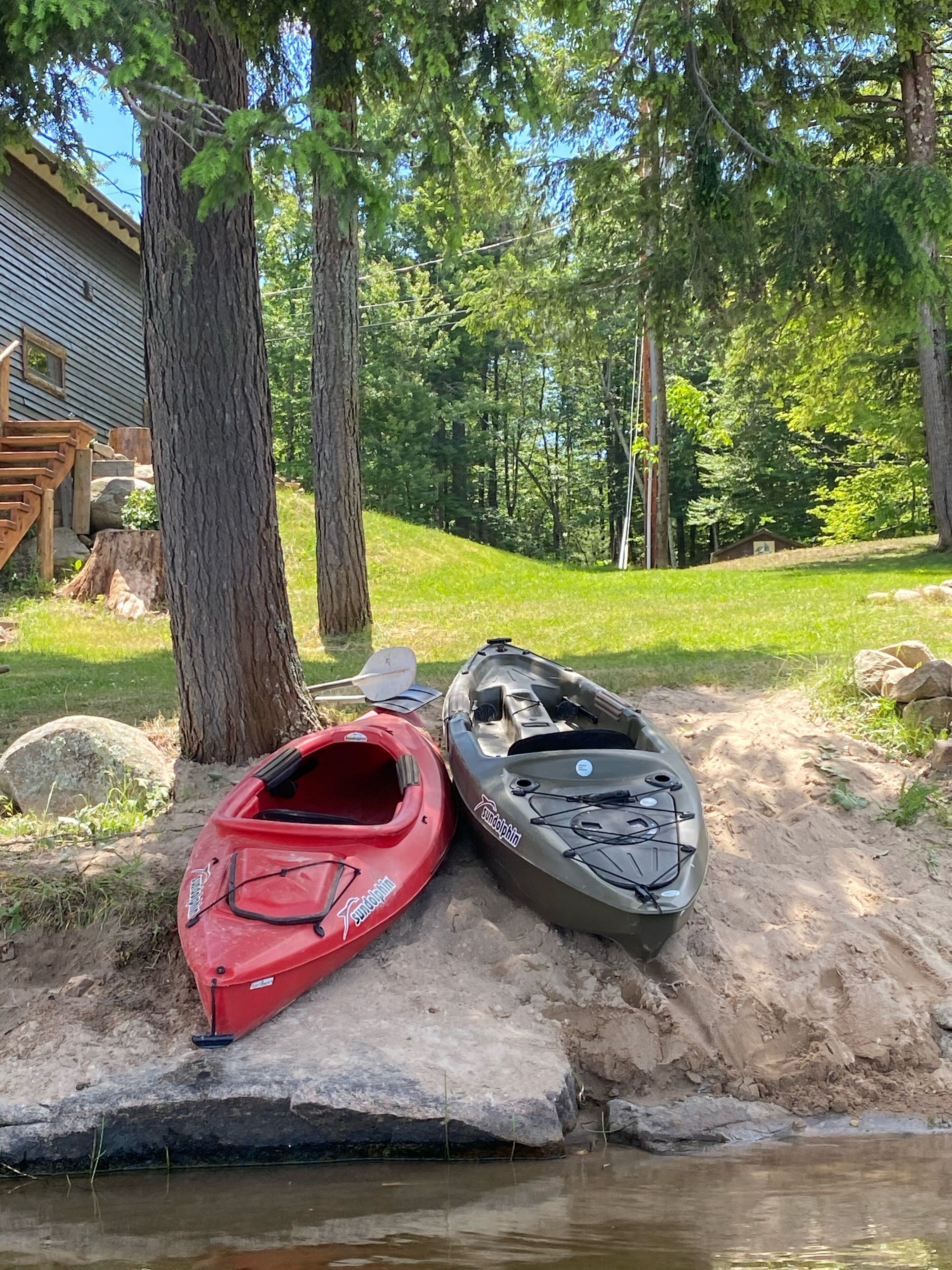 Dos kayaks en una orilla arenosa con un edificio pequeño al fondo.