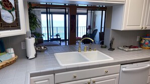 A kitchen with a white sink, two gold faucets, and a view of the ocean through large glass doors. - Seabatical at The Gulf Tower, Beautiful Beachfront Condo (Gulf Shores)