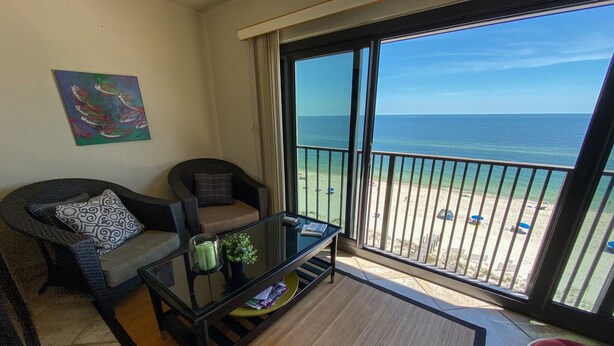 A balcony with a view of the sea, a glass table, two chairs, and a painting on the wall. - Seabatical at The Gulf Tower, Beautiful Beachfront Condo (Gulf Shores)