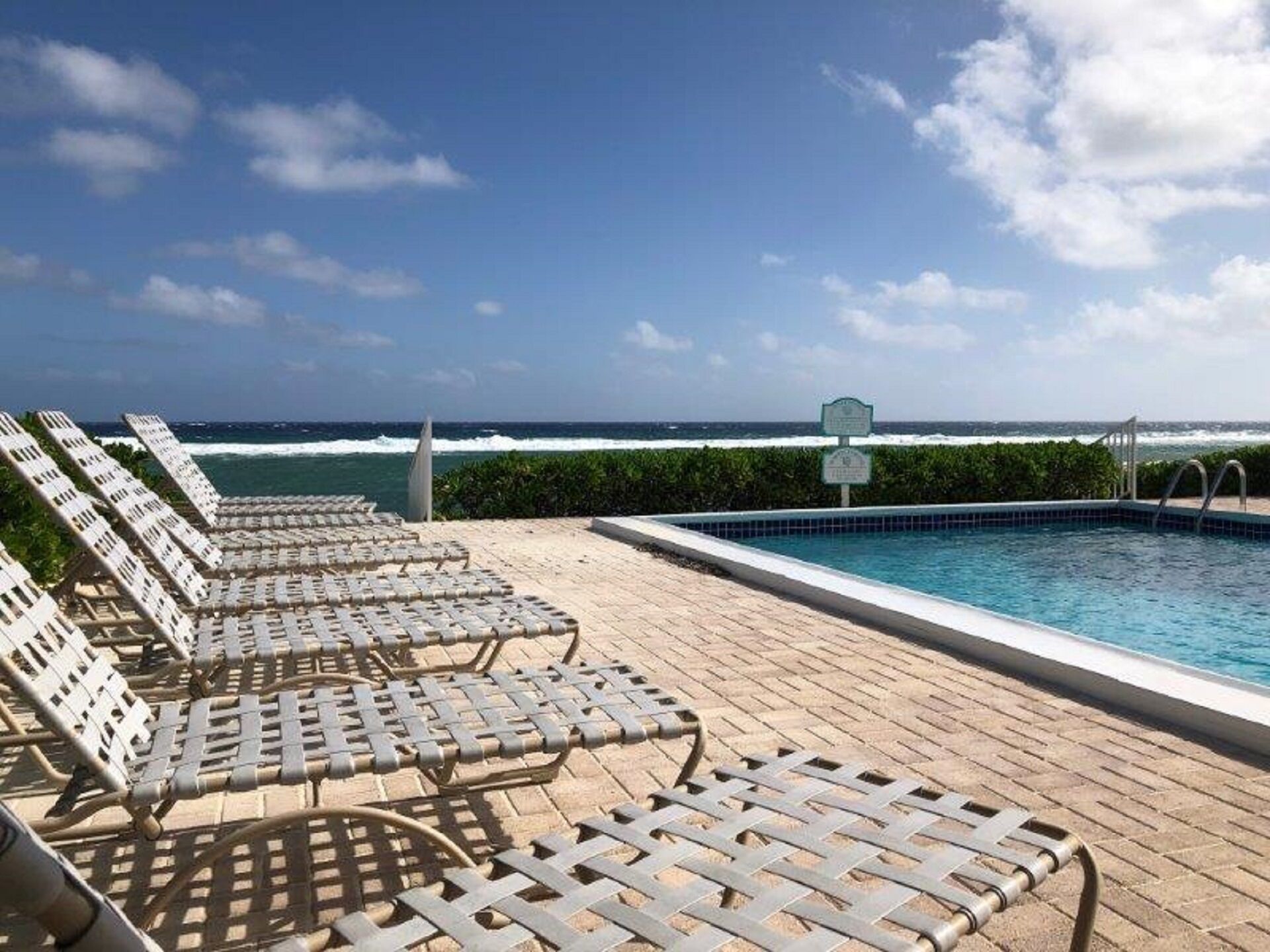 Zona de piscina con sillas de descanso y vista al océano.