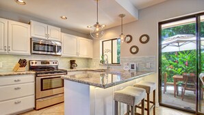 A modern kitchen with white cabinets, stainless steel appliances, and a large island with bar stools. - Beautiful Three Bedroom Townhouse at Napili Bay (Lahaina)