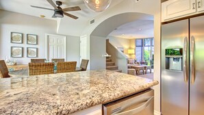 A kitchen with granite countertops, stainless steel appliances, wicker furniture, and a staircase leading to a dining area. - Beautiful Three Bedroom Townhouse at Napili Bay (Lahaina)