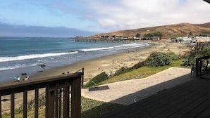 A beach with a wooden deck overlooking the ocean, a pier extending into the water, and hills in the background. - Best Location! Best View! - EXCLUSIVELY ON VRBO (Cayucos)