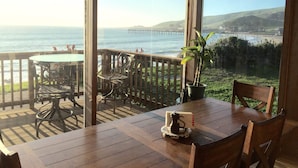 A wooden deck with a table and chairs, a potted plant, and a view of the ocean and pier. - Best Location! Best View! - EXCLUSIVELY ON VRBO (Cayucos)