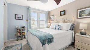 Une chambre à coucher avec un lit, des tables de chevet, une bibliothèque et une fenêtre avec des rideaux.