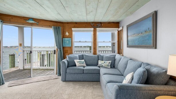 Un salon chaleureux avec un canapé d’angle gris, un plafond en bois et une grande fenêtre donnant sur une terrasse.