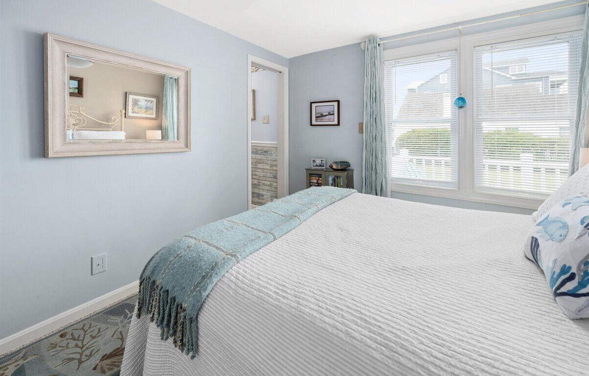 A bedroom with a large bed, a mirror, a dresser, and a window with blinds.