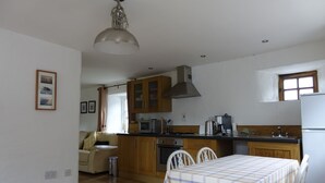 Una cucina compatta con mobili in legno, un forno a microonde, un fornello e un frigorifero. È presente un tavolo da pranzo con tovaglia a quadri.