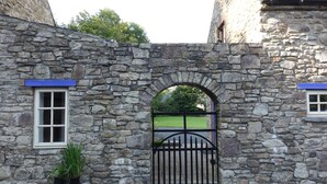 Un edificio in pietra con un'ampia porta ad arco, una pianta in vaso e vista su un prato verde attraverso il cancello.