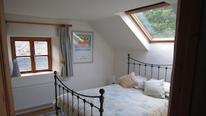 Una camera da letto con soffitto spiovente, un letto con biancheria da letto floreale, un termosifone, una finestra con tende e un quadro appeso al muro.