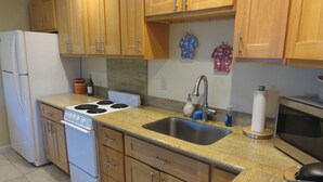 A kitchen with wooden cabinets, a white stove, a sink, and a microwave. - Footsteps to Hawaii's Best Beach  (Kailua)