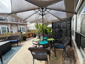An outdoor patio with wicker furniture, a round table, and a large umbrella providing shade. - Tropical Retreat! Just steps to the surf & sunsets! (San Diego)