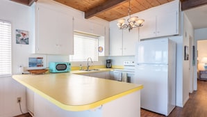 Una cocina moderna con una isla central, armarios blancos, un microondas de estilo vintage y un refrigerador de acero inoxidable.