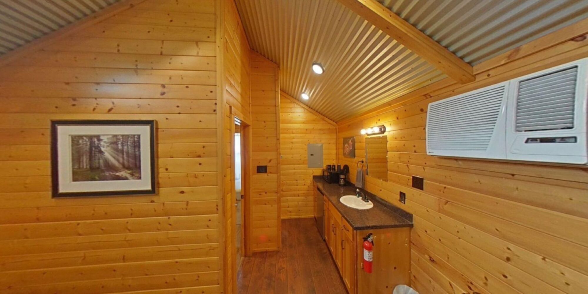 A wooden cabin interior with a framed picture, a sink, and a fire extinguisher.