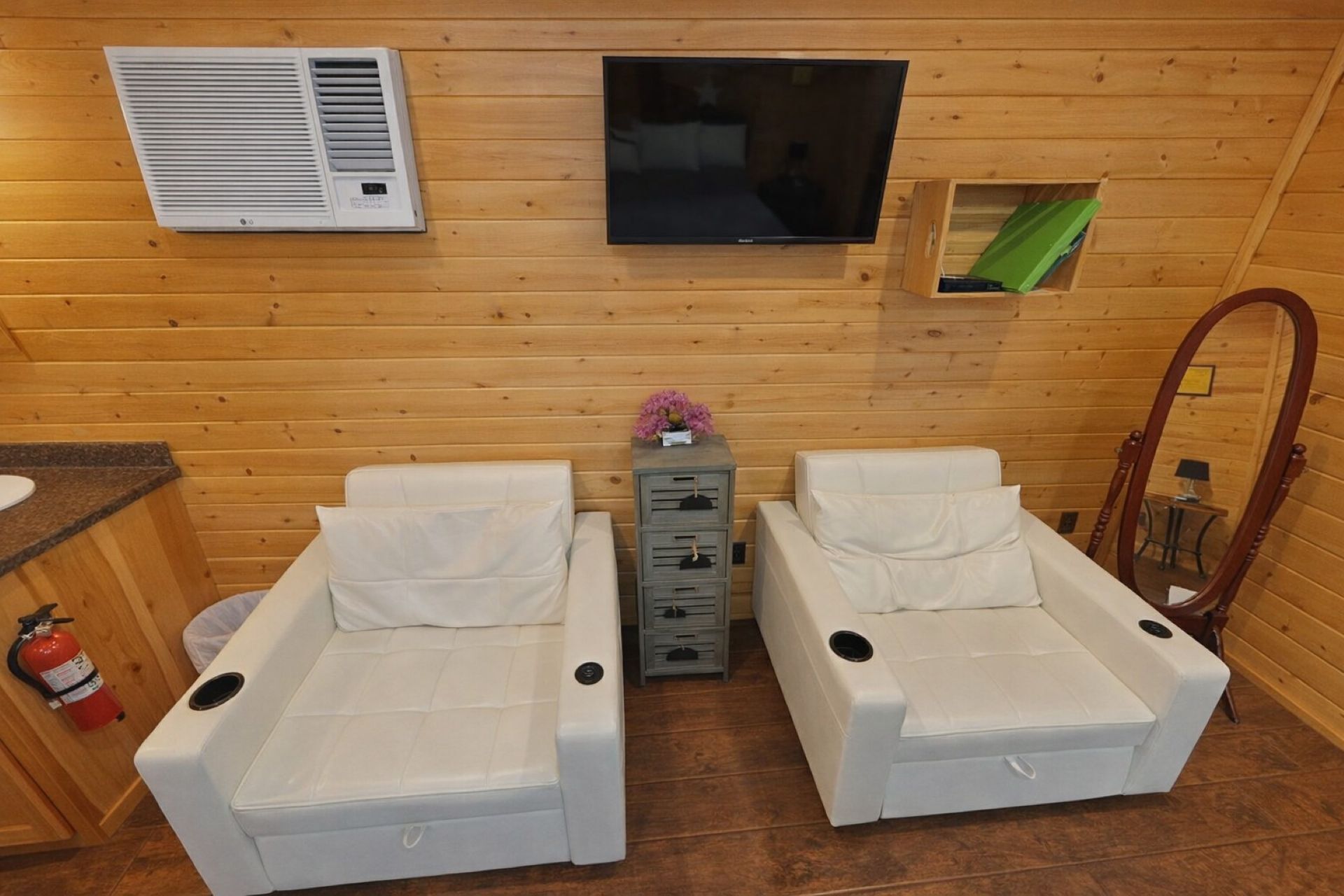 Una habitación con dos sillones de masaje blancos, un televisor, un mueble pequeño y una pared de madera.
