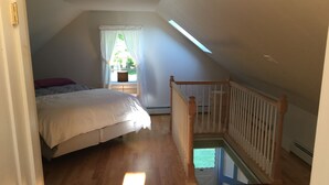 Quarto com cama, janela com cortinas, escada de madeira e vista para o exterior.