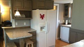 Uma cozinha compacta com bancadas de granito, geladeira branca, banquetas de madeira e lava-louças embutida.