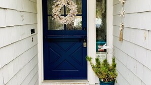 Une porte d’entrée bleue ornée d’une guirlande, un paillasson sur lequel est écrit « SOYEZ LES BIENVENUS », et une plante en pot placée à côté de la porte.
