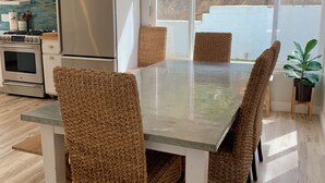 Une cuisine moderne avec un coin repas, comprenant une grande table, des chaises en osier et un luminaire suspendu.