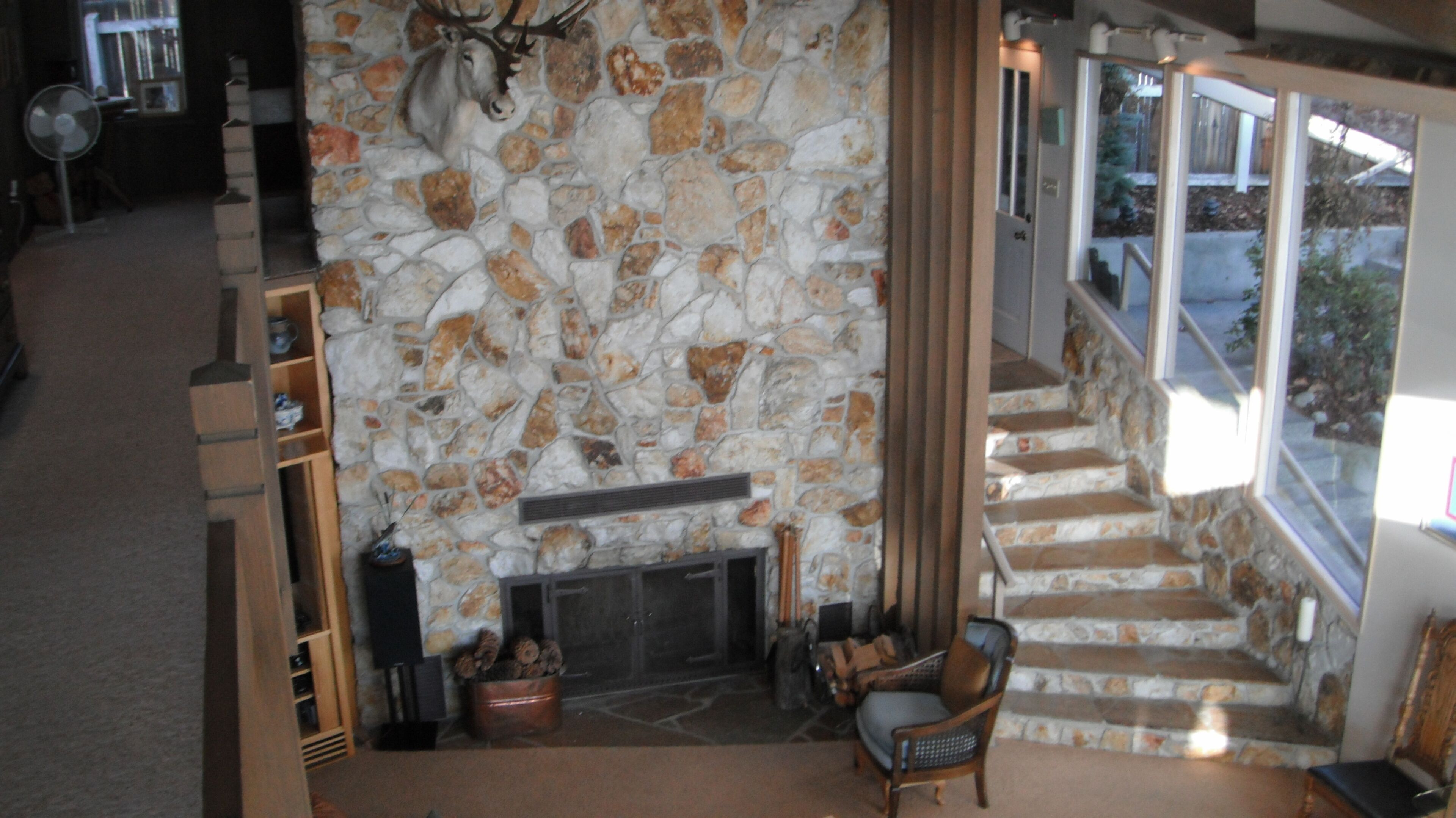 A stone fireplace with a deer head, a fireplace, and a chair in a room with a stone wall.