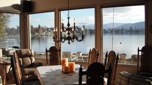 A room with a large window overlooking a lake, a chandelier, and a table with candles. - Beautiful Lakefront Home (Manson)