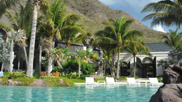 A poolside area with lounge chairs, palm trees, and a mountain backdrop. - Architecturally Designed Villa in Paradise, Quiet Beach & Blue Water Views (Turtle Beach)