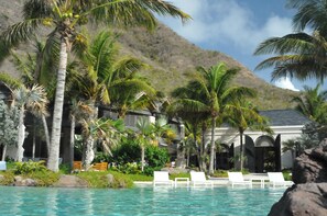 Un espace aménagé au bord de la piscine, avec des chaises longues, des palmiers et une chaîne de montagnes en arrière-plan.
