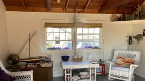 A cozy room with a wooden ceiling, a white wicker chair with a lobster cushion, a small table with books and a globe, and a window with purple flowers. - The Quintessential Traditional Nantucket Vacation! (Nantucket)
