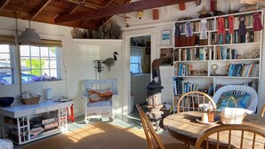 A cozy room with a wooden ceiling, wicker furniture, a bookshelf filled with books, and a vintage stove. - The Quintessential Traditional Nantucket Vacation! (Nantucket)