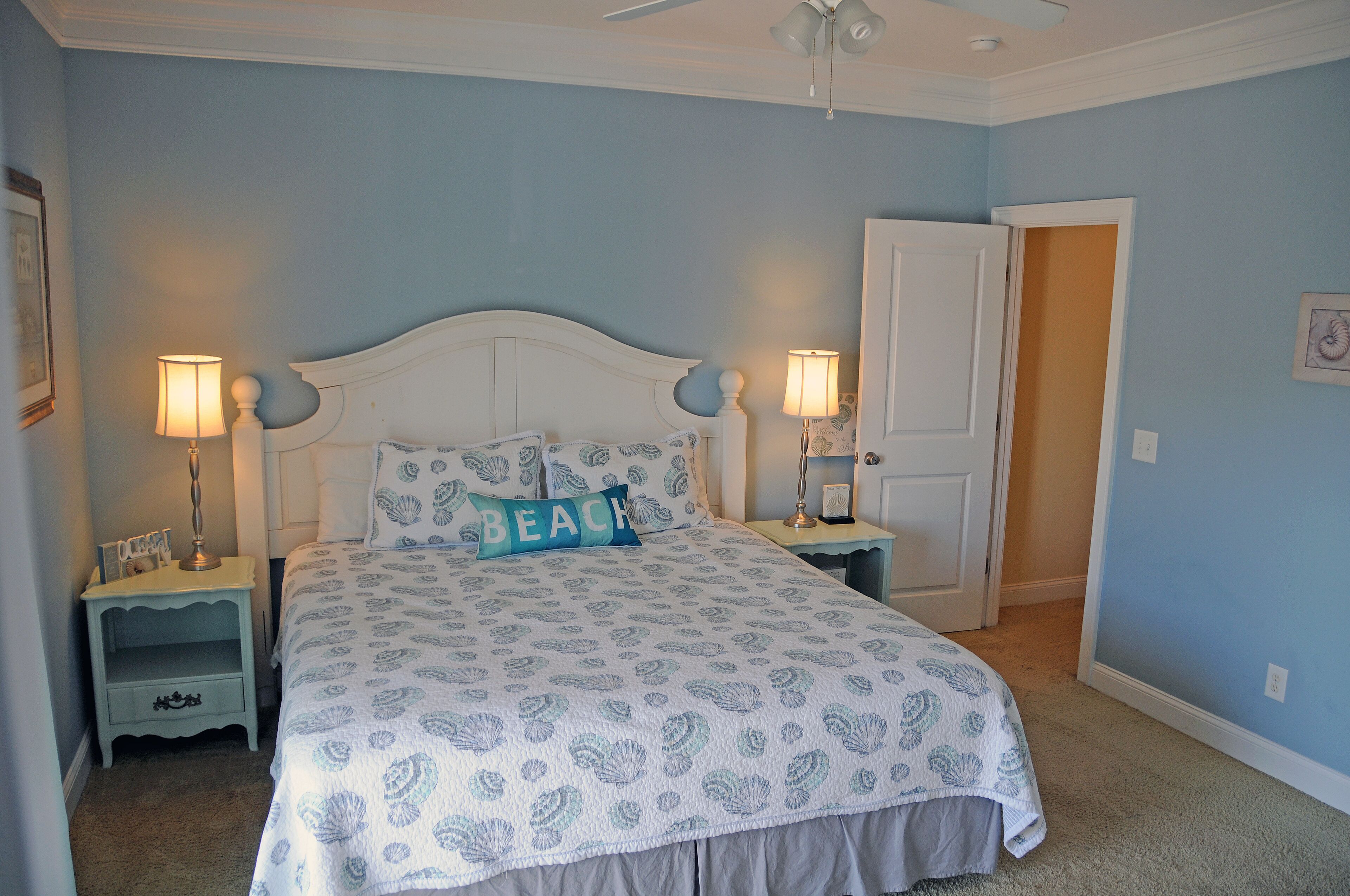 A bedroom with a bed, two bedside tables, a nightstand, a door, and a ceiling fan.