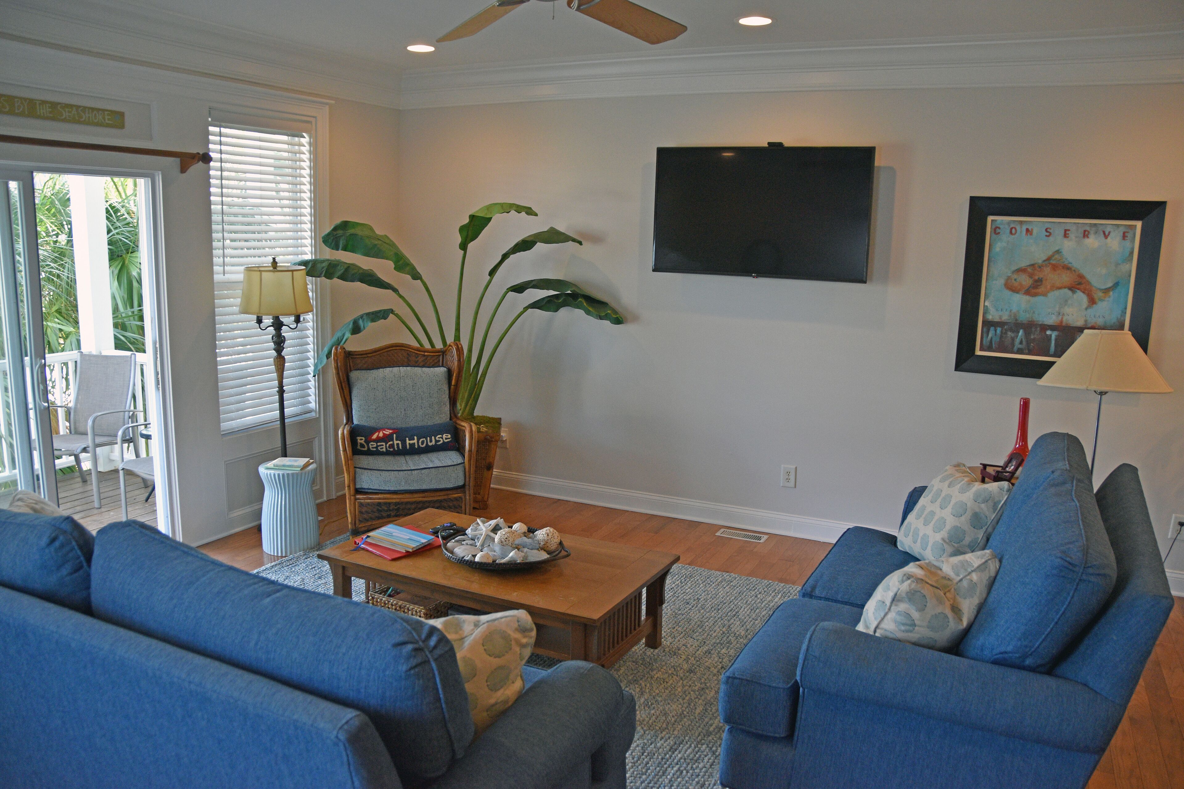A living room with a ceiling fan, a large plant, and a framed picture on the wall.
