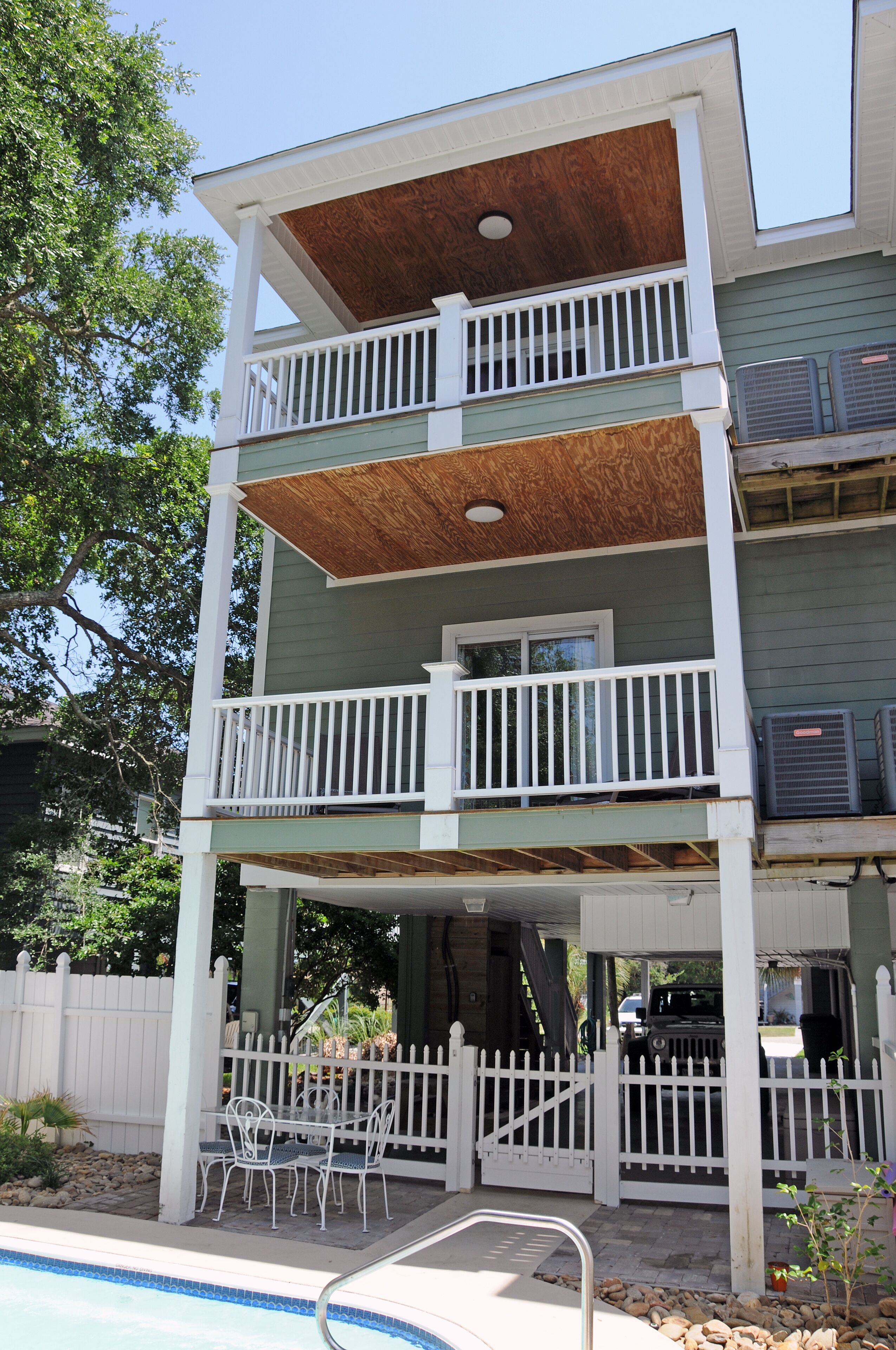 A two-story building with a wooden deck, a pool, and a white fence.