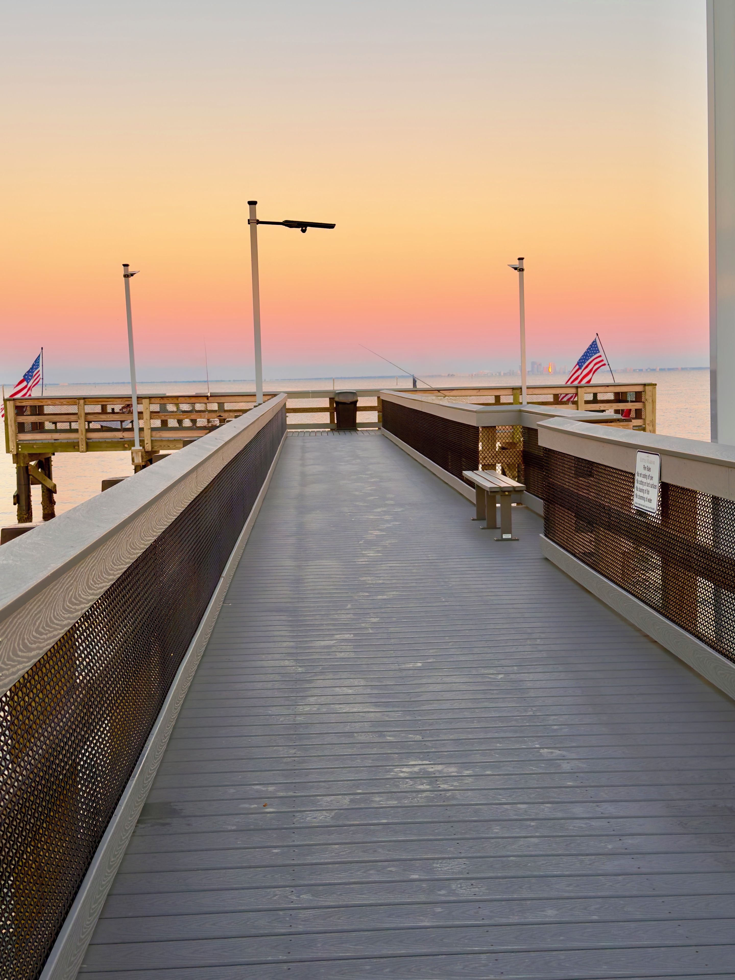 A wooden pier extending into a body of water with a sunset in the background.