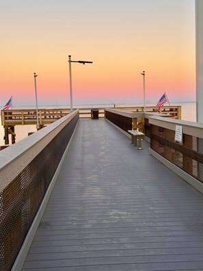 Un muelle de madera se adentra en un cuerpo de agua con un atardecer de fondo.