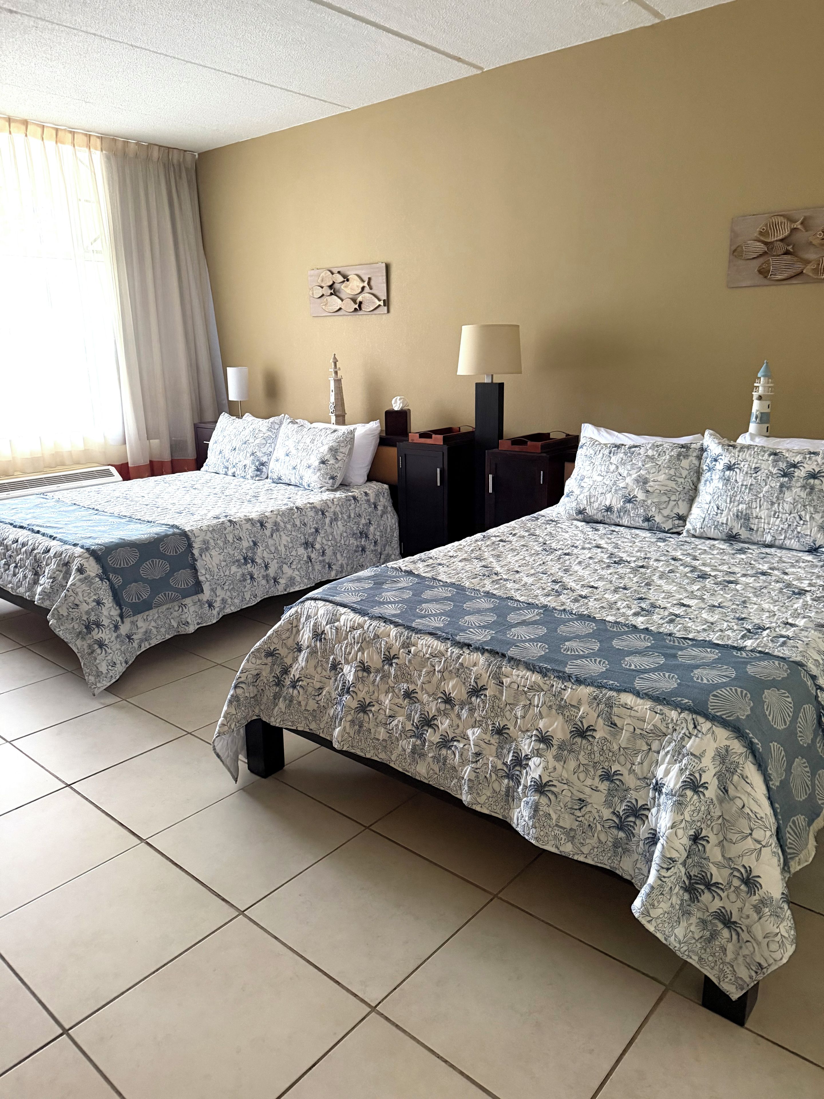 A hotel room with two beds, a nightstand, a lamp, and a decorative wall piece.
