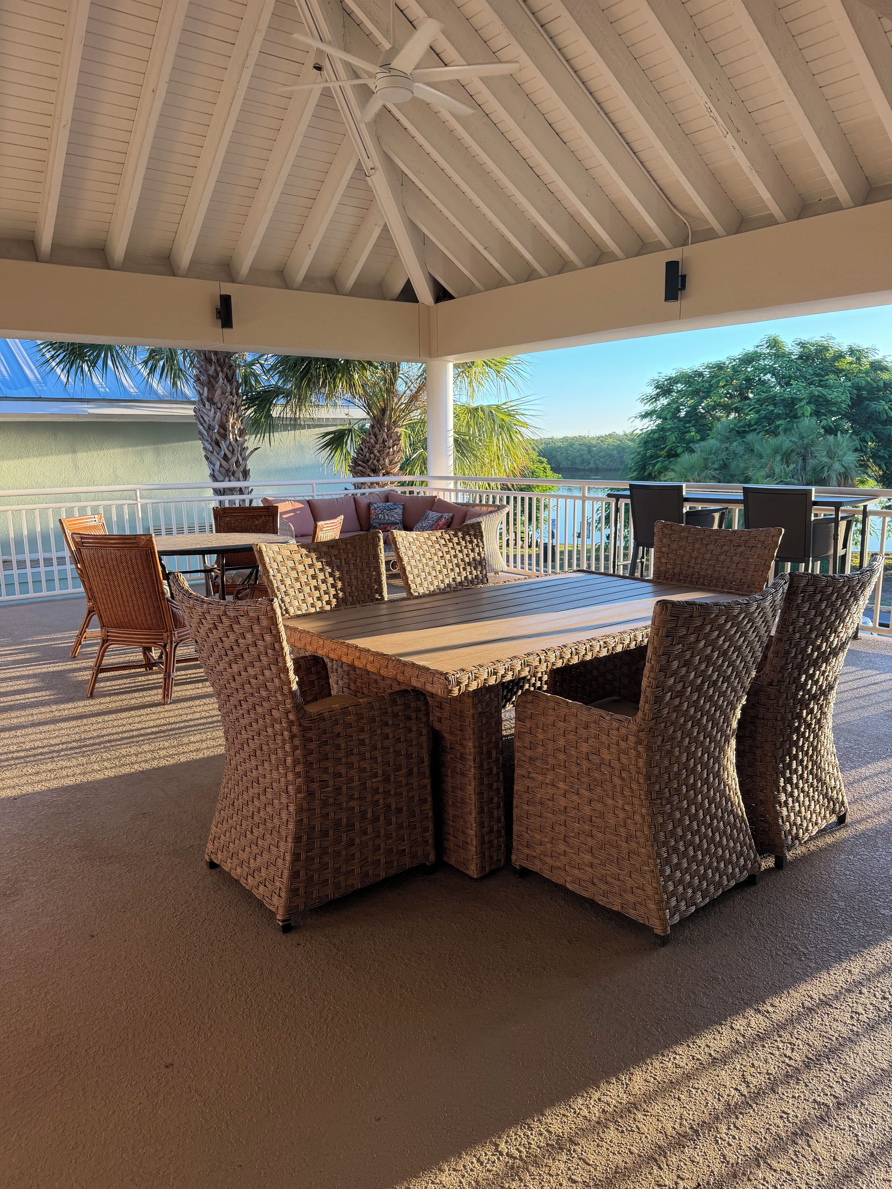 Une terrasse extérieure avec une table et des chaises, un ventilateur de plafond et une vue sur l’eau.