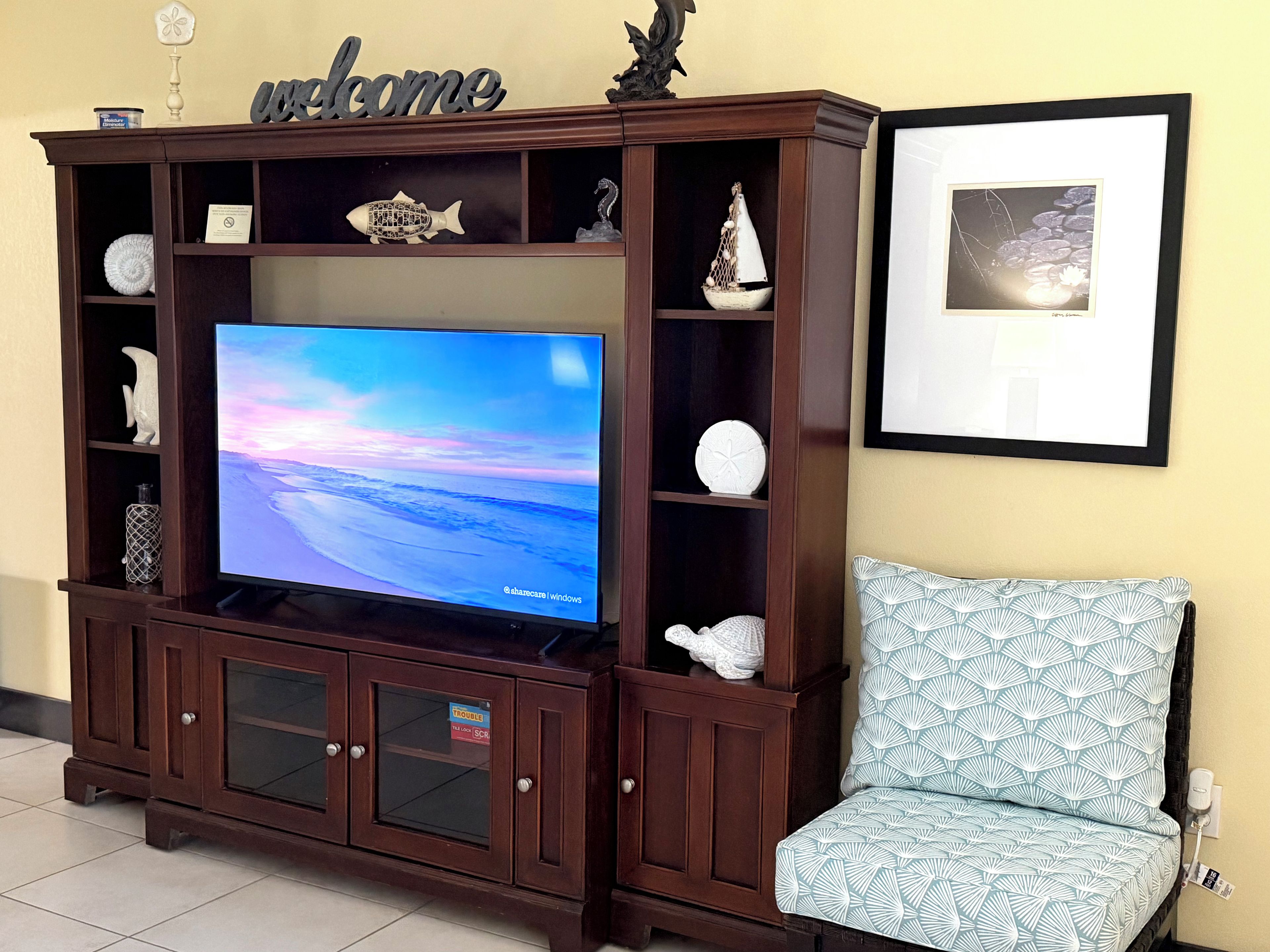 A wooden entertainment center with a flat-screen TV, a framed picture on the wall, and a patterned armchair.