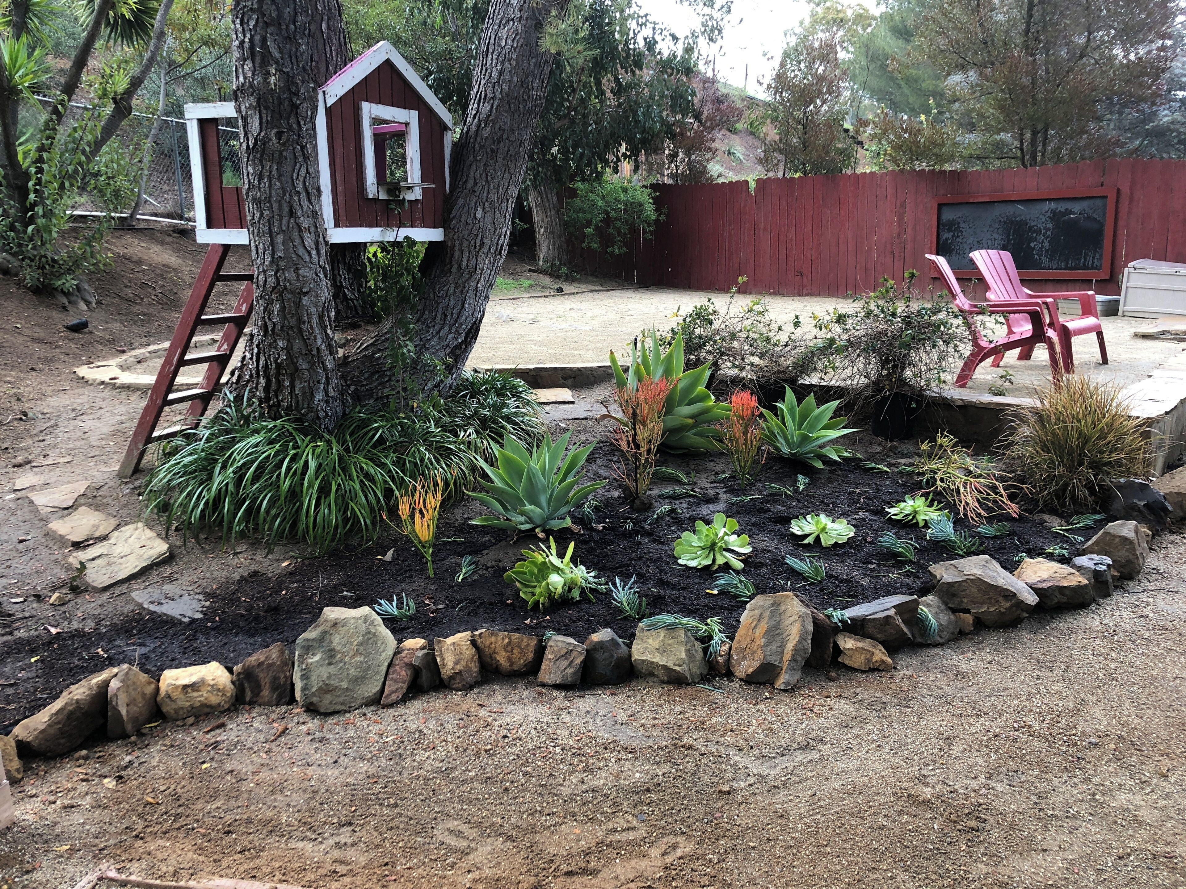 A garden with a birdhouse, a wooden ladder, and a red chair.
