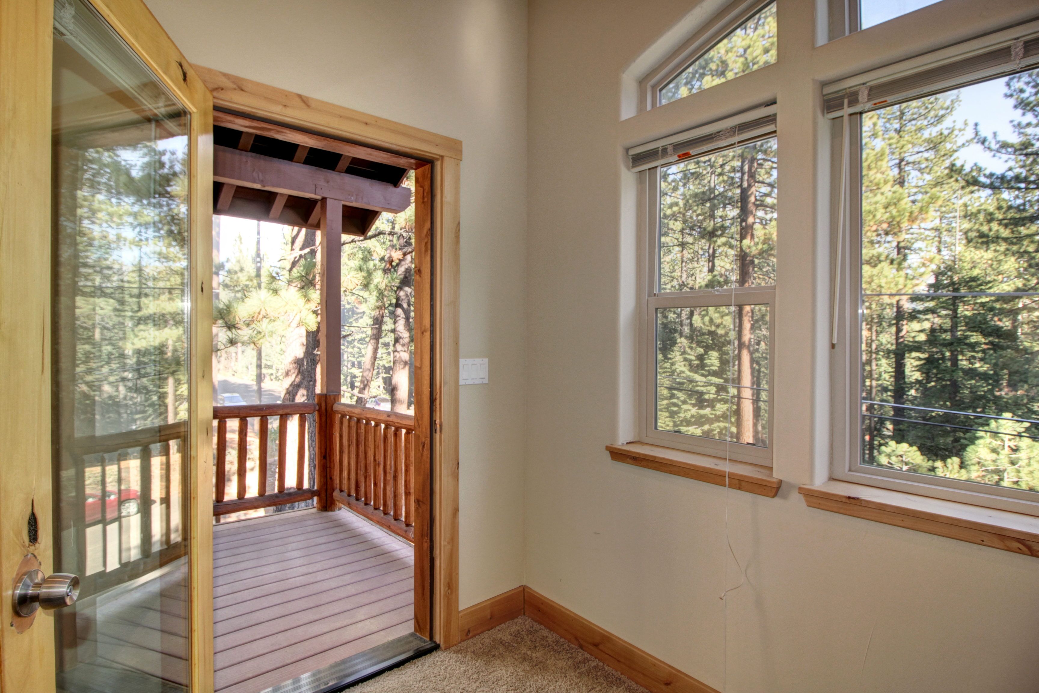 A room with a wooden deck, large windows, and a view of a forest.
