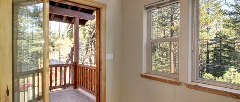 A room with a wooden deck, large windows, and a view of a forest.