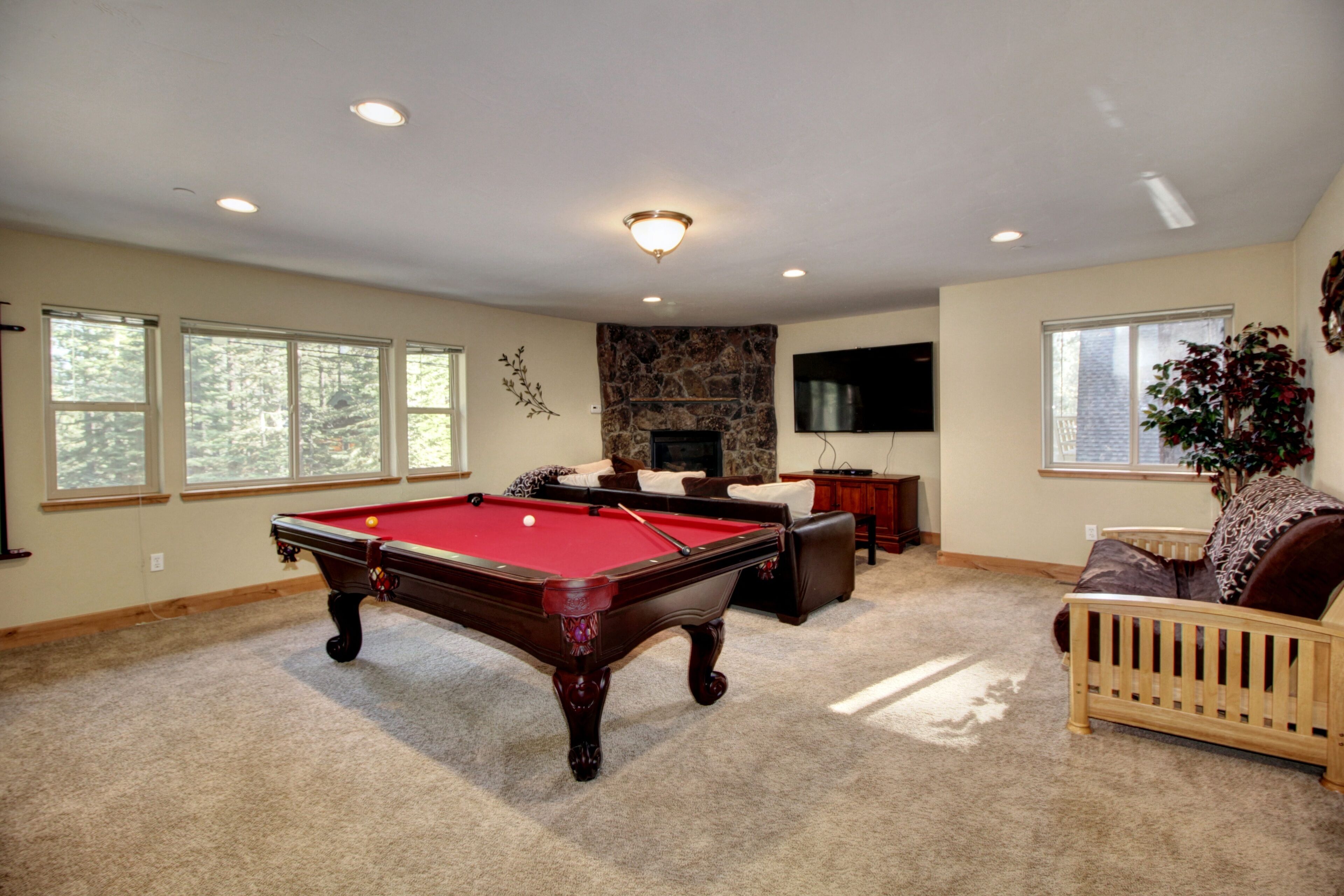 A spacious living room with a pool table, comfortable seating, a fireplace, and large windows.