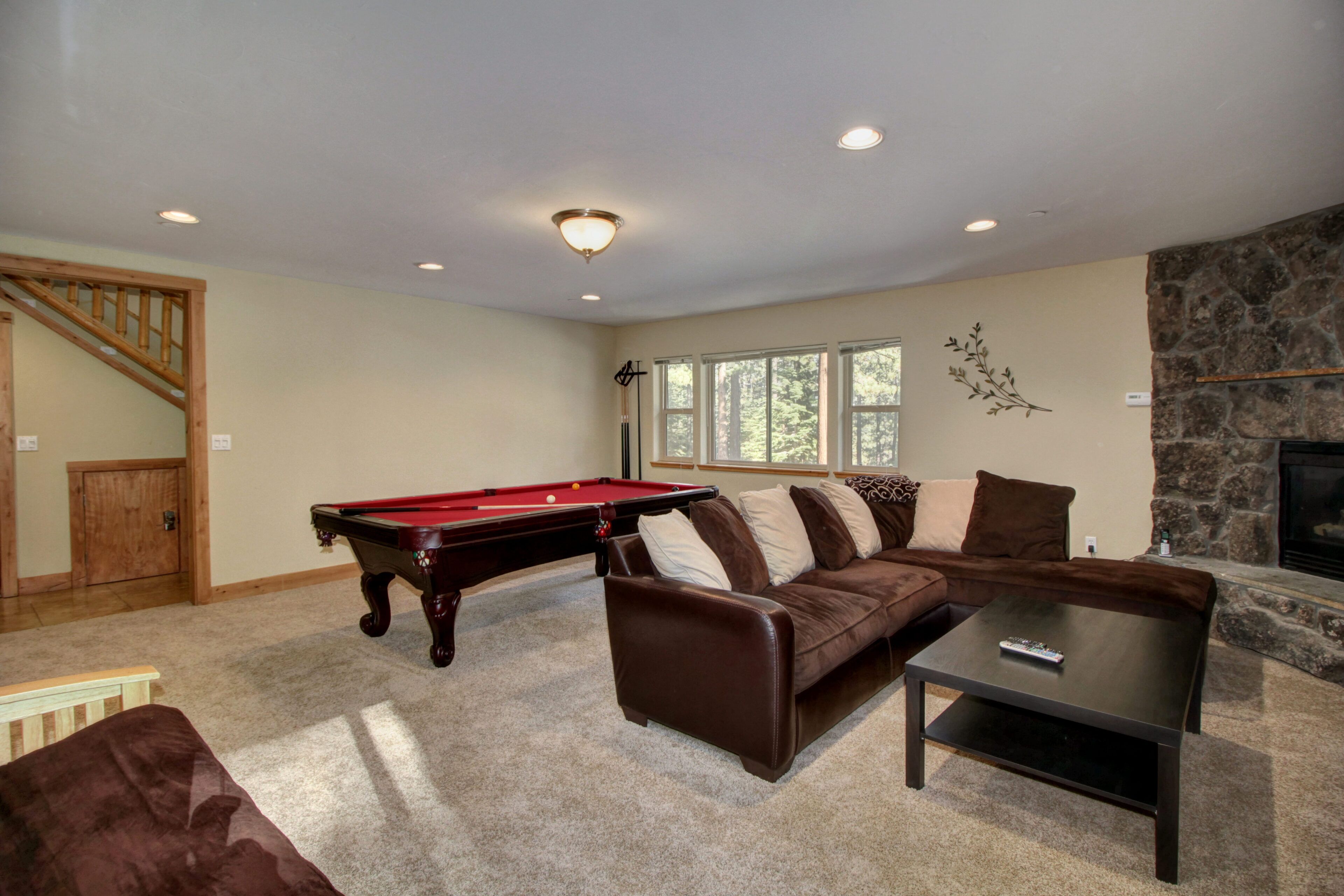 A living room with a pool table, a brown leather sofa, a coffee table, and a stone fireplace.