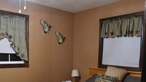 A bedroom with a bed, a ceiling fan, a window with curtains, and wall decorations.