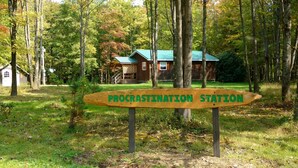 A wooden sign with the text "Procrastination Station" in a forested area with a building in the background.