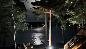 Vista notturna di un pontile sul lago con una scala in legno, circondato da alberi, e un molo che si protende nell'acqua.