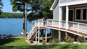 Una casa con veranda che si affaccia su un lago, circondata da alberi e un prato curato.